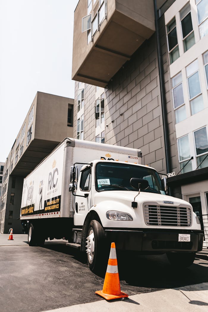 A moving truck parked outside a modern apartment building in an urban setting.